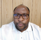 Meshack Dludlu headshot photo, wearing a white shirt, in front of a wood panel wall